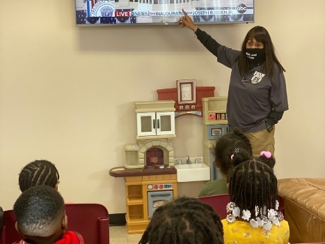 a teacher points to a tv as her students watch attentively